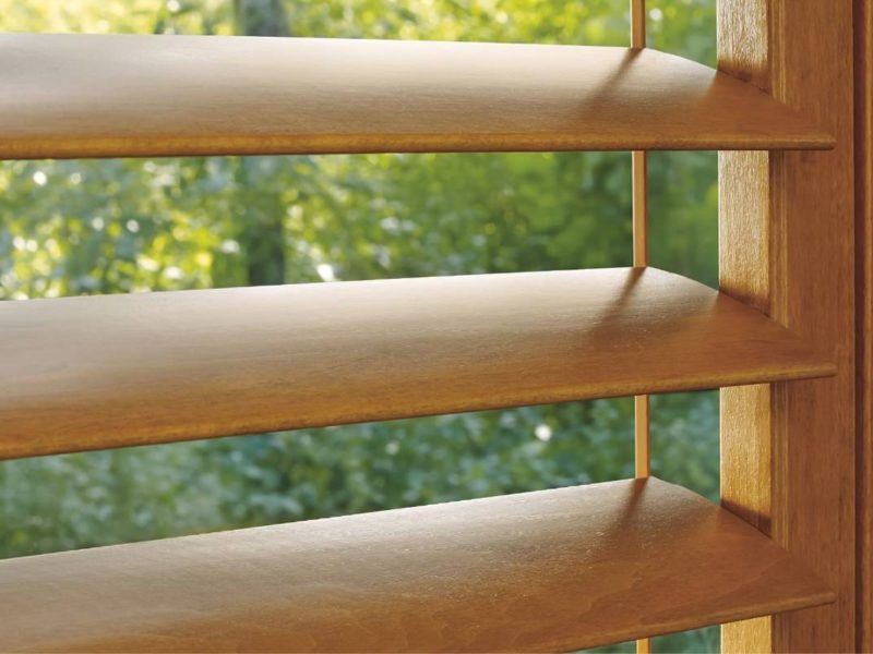 Close-up of open Hunter Douglas Heritance® Wood Shutters on a window overlooking a yard with green trees